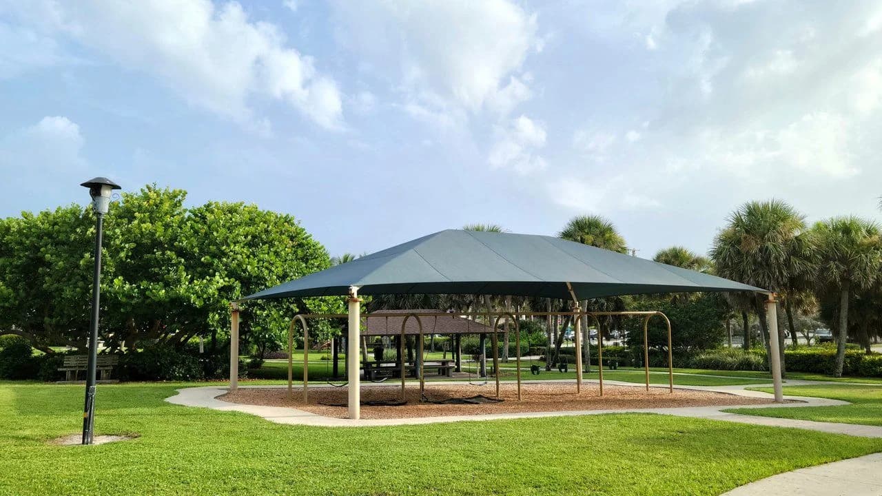 Public park playground with a swing set under a shade canopy; no people visible.