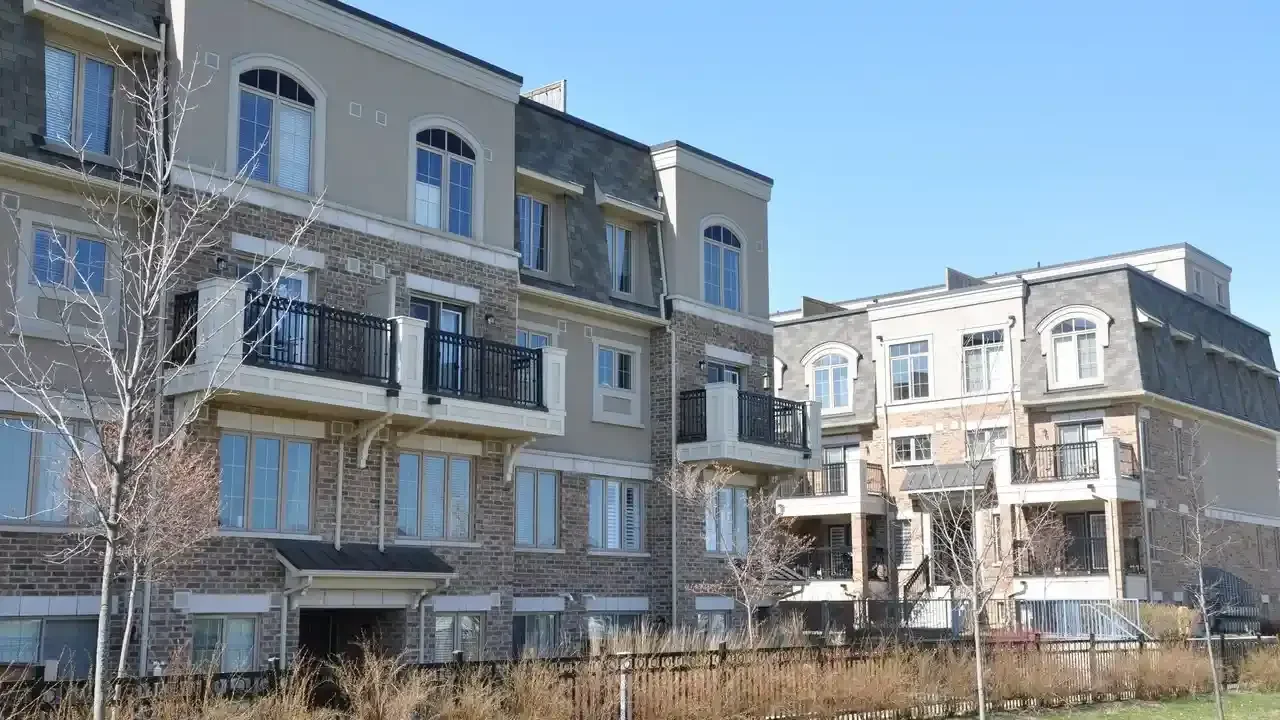 Modern stacked townhouses with brick facades and black-railed balconies on a sunny day in Oakville, Ontario.