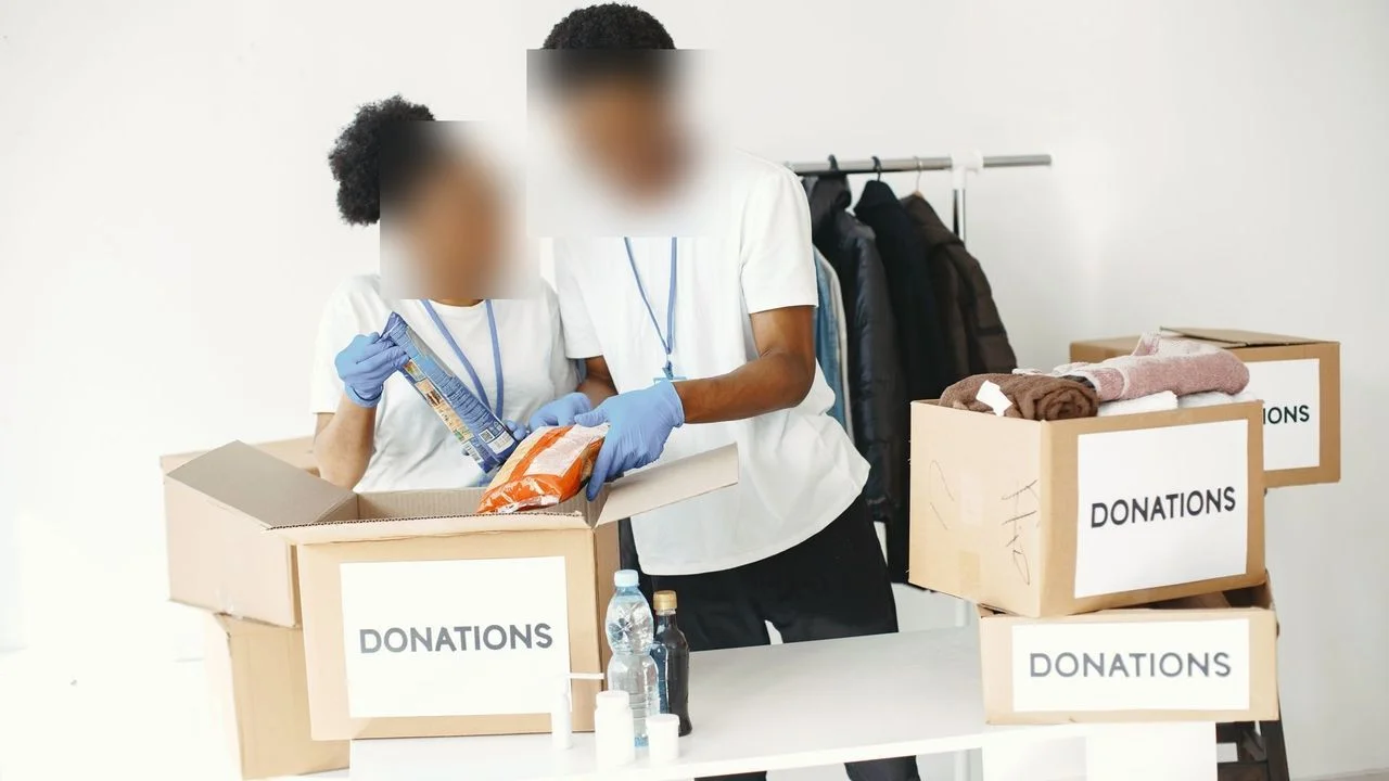 Two volunteers packing food and supplies into cardboard boxes labelled 'DONATIONS'.